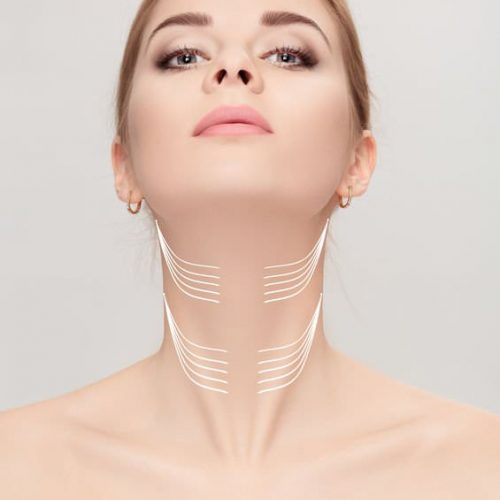 woman with arrows on her face over grey background. neck lifting concept. correction of double chin